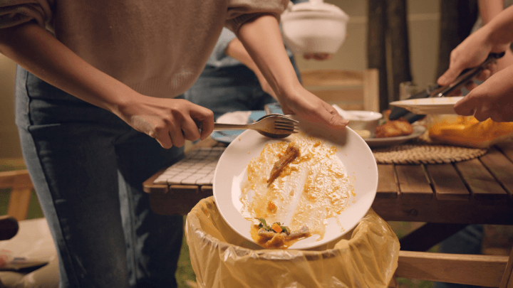 A group of individuals disposing of leftover food into a plastic trash bag after a home party, illustrating the concept of reducing household waste for a greener, eco-friendly lifestyle and earth conservation.