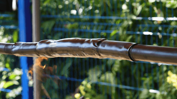 Wire isolation with heat shrink tubing in front of a blue fence against a background of green trees. Illustrating the process of wire protection using heat shrink tubing.