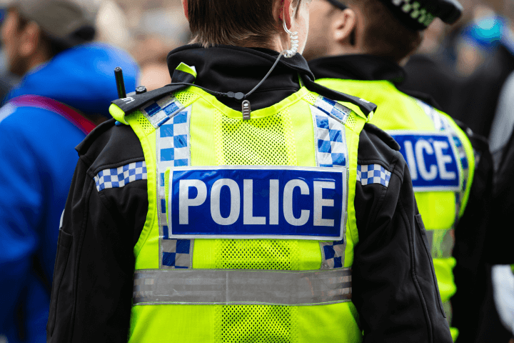 Leeds, United Kingdom – May 05, 2019: A law enforcement officer in a yellow vest bearing the word 'police' on the back, participating in the Tour de Yorkshire event in the city center of Leeds.