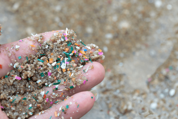 Hands reveal microplastic waste mixed with seaside sand, indicating contamination.