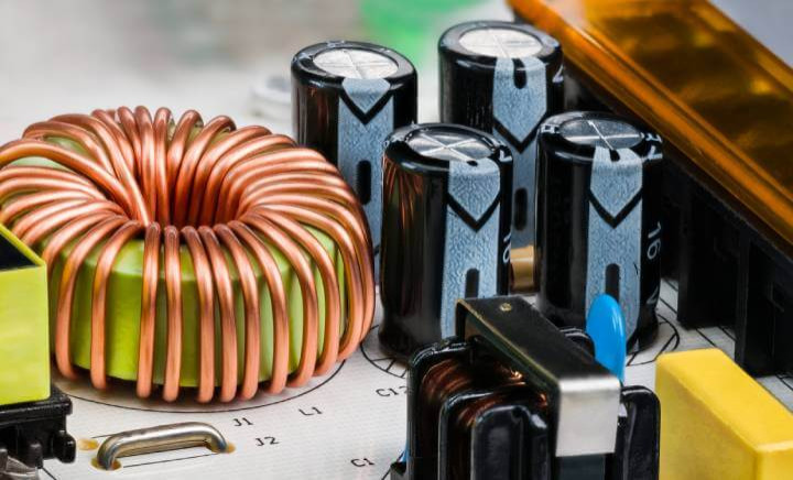 Close-up view of a coil encircled by copper wire on a white printed circuit board, an essential component of a switch-mode power supply's electromagnetic induction choke.