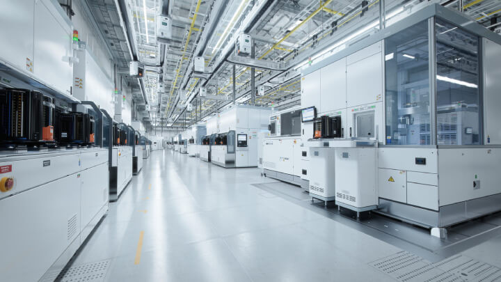 Wide-angle view of a brightly lit advanced semiconductor production facility, featuring a cleanroom environment with an operational overhead wafer transfer system.